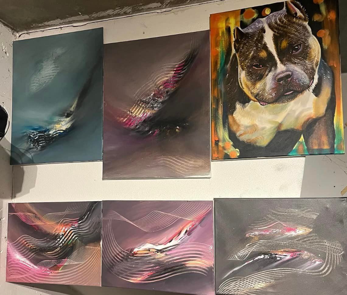 Schilderijen aan een witte muur. Het kunstwerk omvat een abstract, kleurrijk hondenportret en een vis.