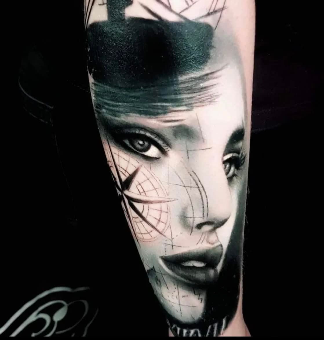 Zwart-witte tatoeage van een vrouwengezicht. De helft toont een kompas, de andere helft is gearceerd.