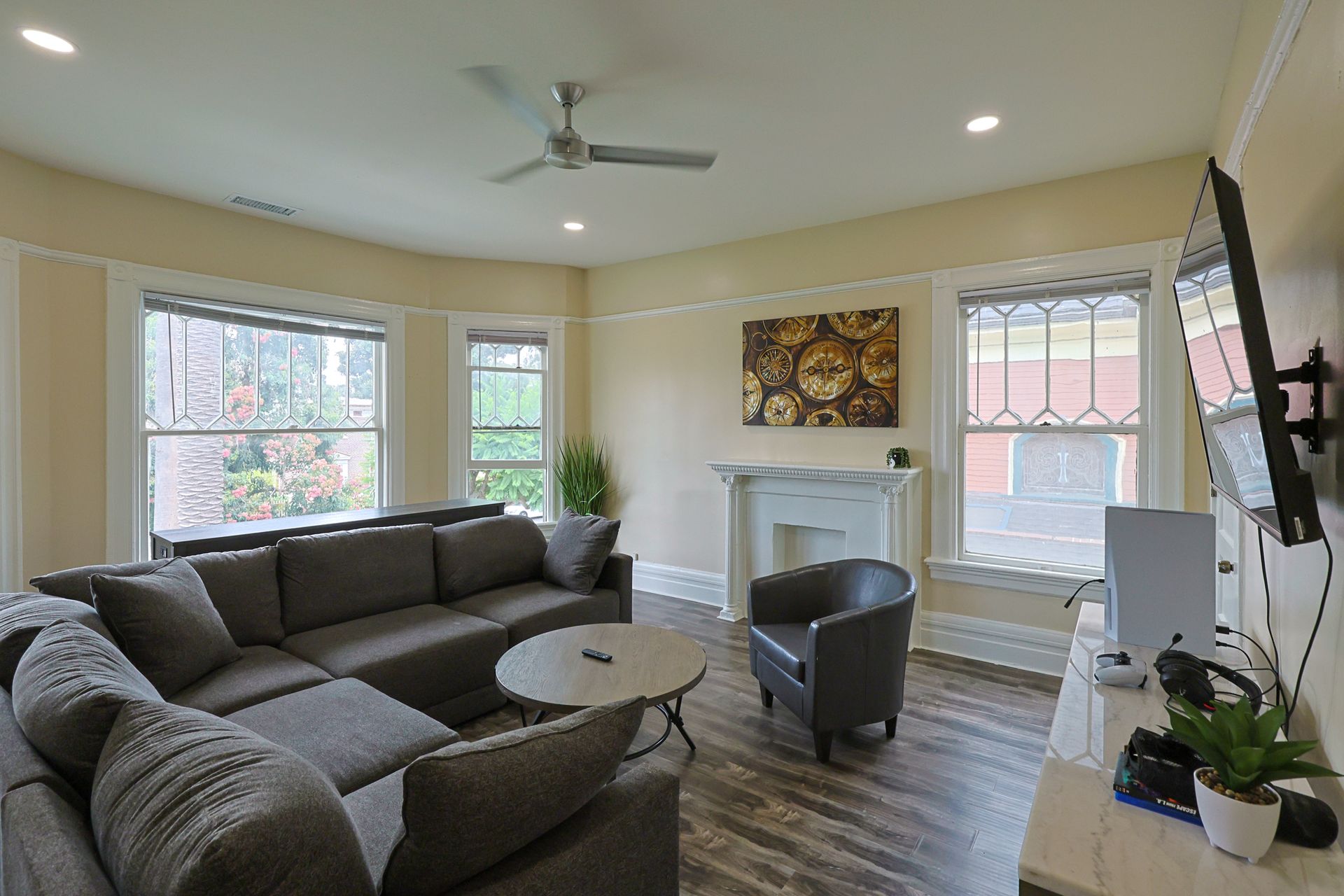 This image showing a beautiful living room with luxurious cough set , round table, smart tv, painting and windows in it.