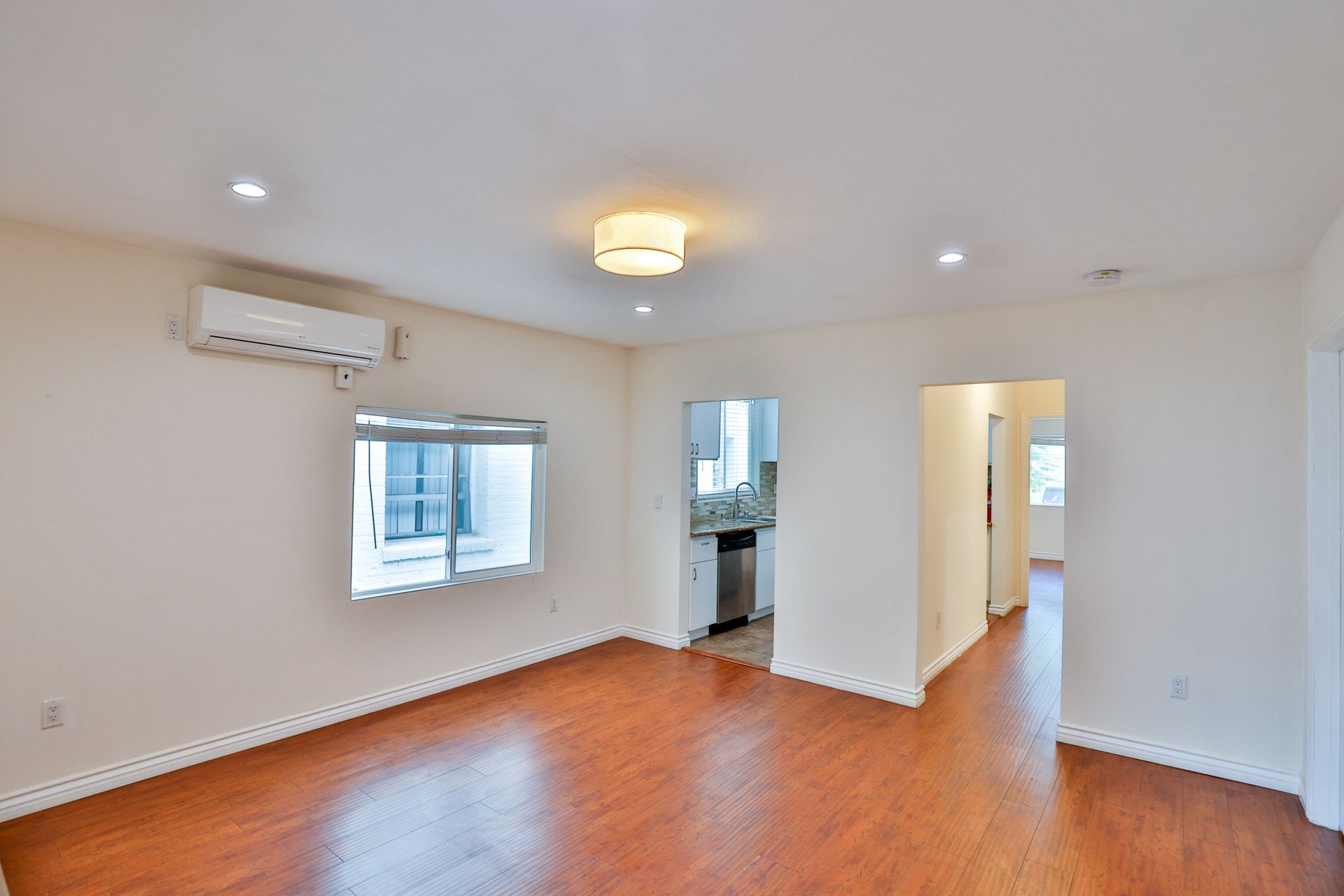 This image showing a spacious room with two doors, hree to four lights on ceiling , AC,and furnished floor in it.