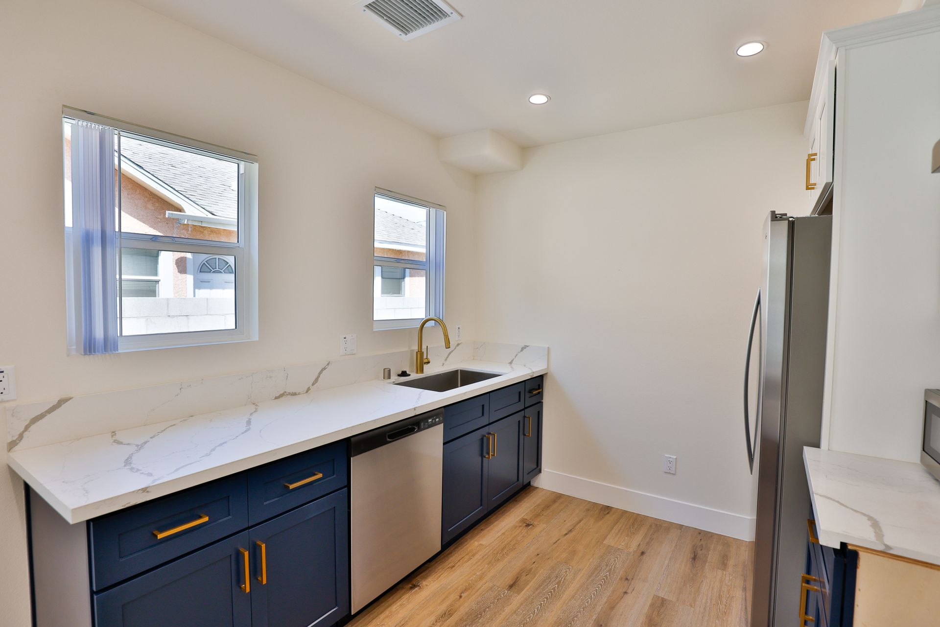 This image shows a kitchen with a stainless steel refrigerator and a wood floor with skin shade color.