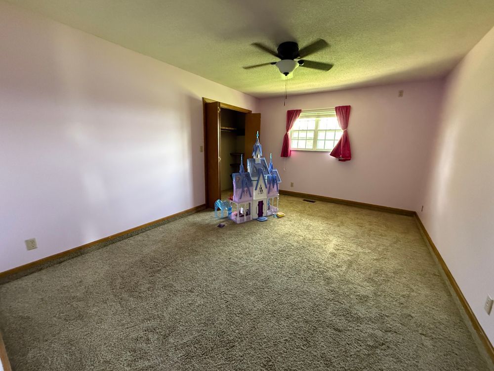 Empty carpeted bedroom with ceiling fan, window, and a small castle playset near the doorway