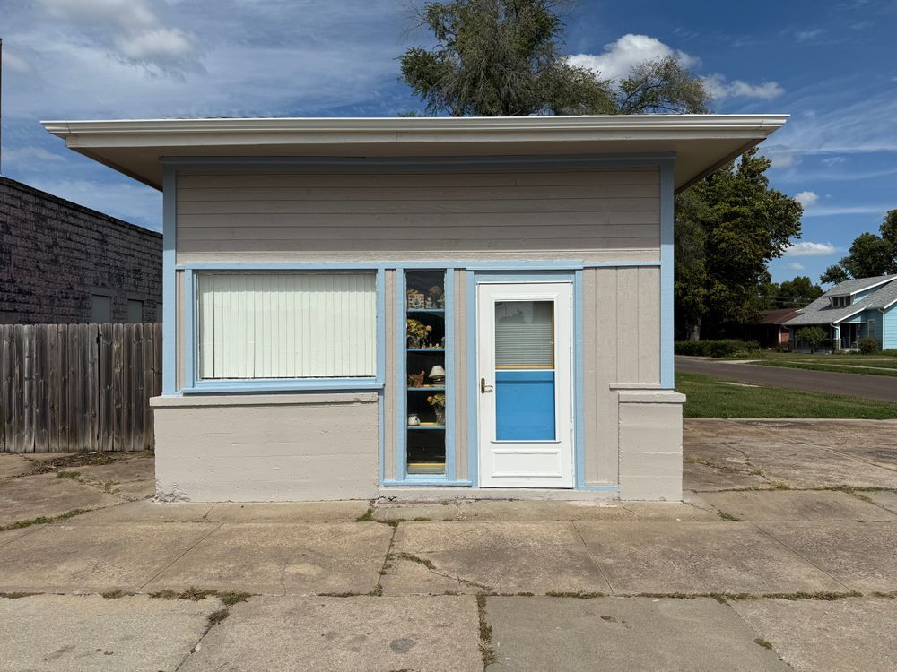 Small beige storefront with white trim and blue front door, seen from the street