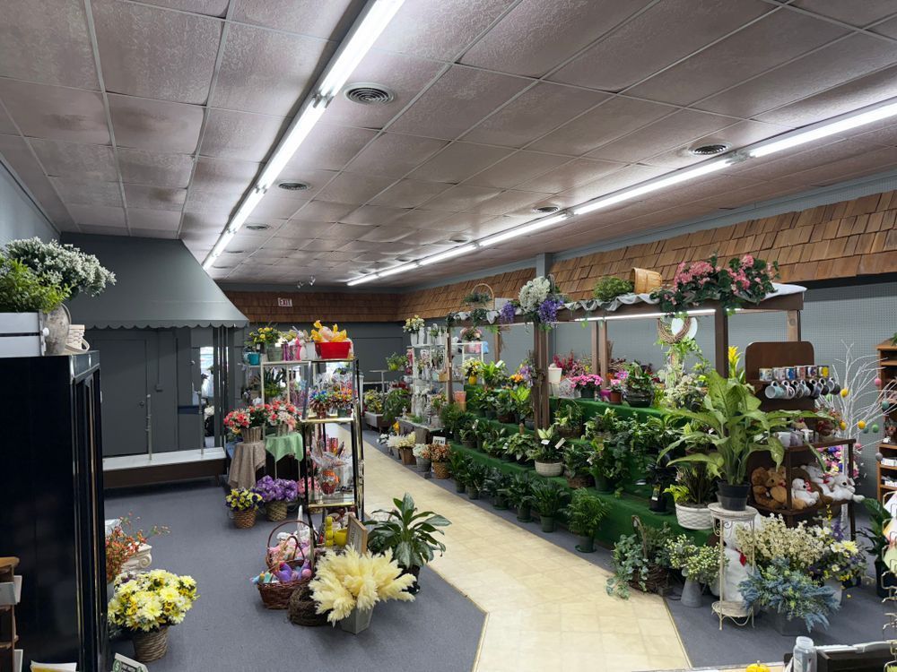 Flower shop interior with rows of potted plants and bouquets along a narrow aisle
