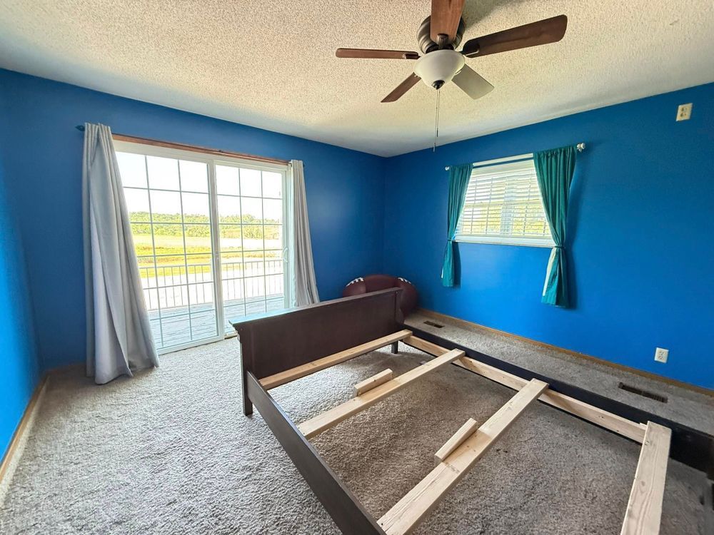Bedroom with blue walls, gray carpet, and an unmade bed frame near a sliding glass door and window.