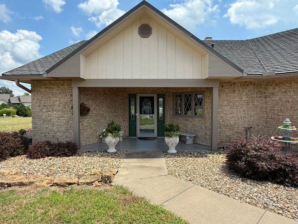 Brick house front entrance with green door, stone walkway, and landscaped yard under a cloudy sky