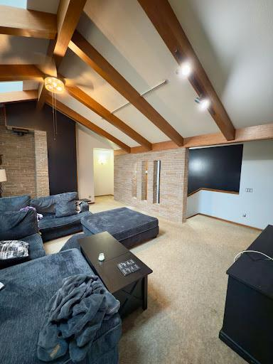 Cozy living room with exposed wood beams, gray sectional sofa, brick fireplace, and wall-mounted TV