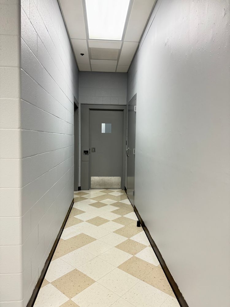 Narrow hallway with gray walls, patterned tile floor, and a closed gray door at the end