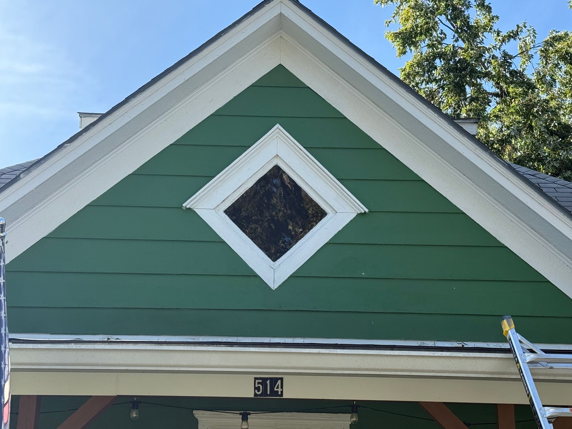 Green house gable with white trim and a diamond window above the front door