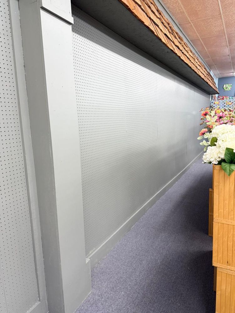Corridor with a perforated white wall, gray carpet, and a wooden flower display on the right.