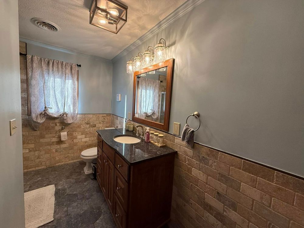 Bathroom with vanity, mirror lights, toilet, and tiled walls in gray and tan tones