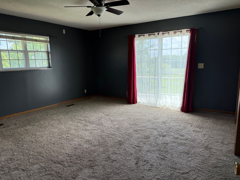 Empty living room with dark blue walls, carpet, ceiling fan, and sliding glass door with red curtains