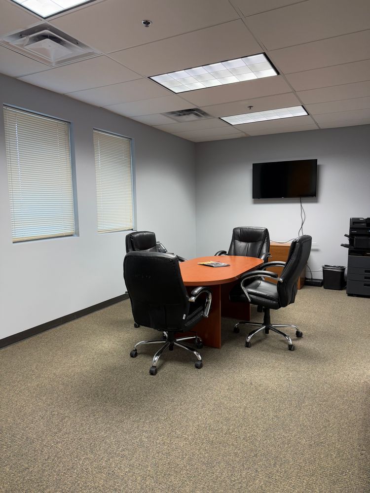 Empty conference room with round table, black chairs, wall-mounted TV, and carpeted floor.