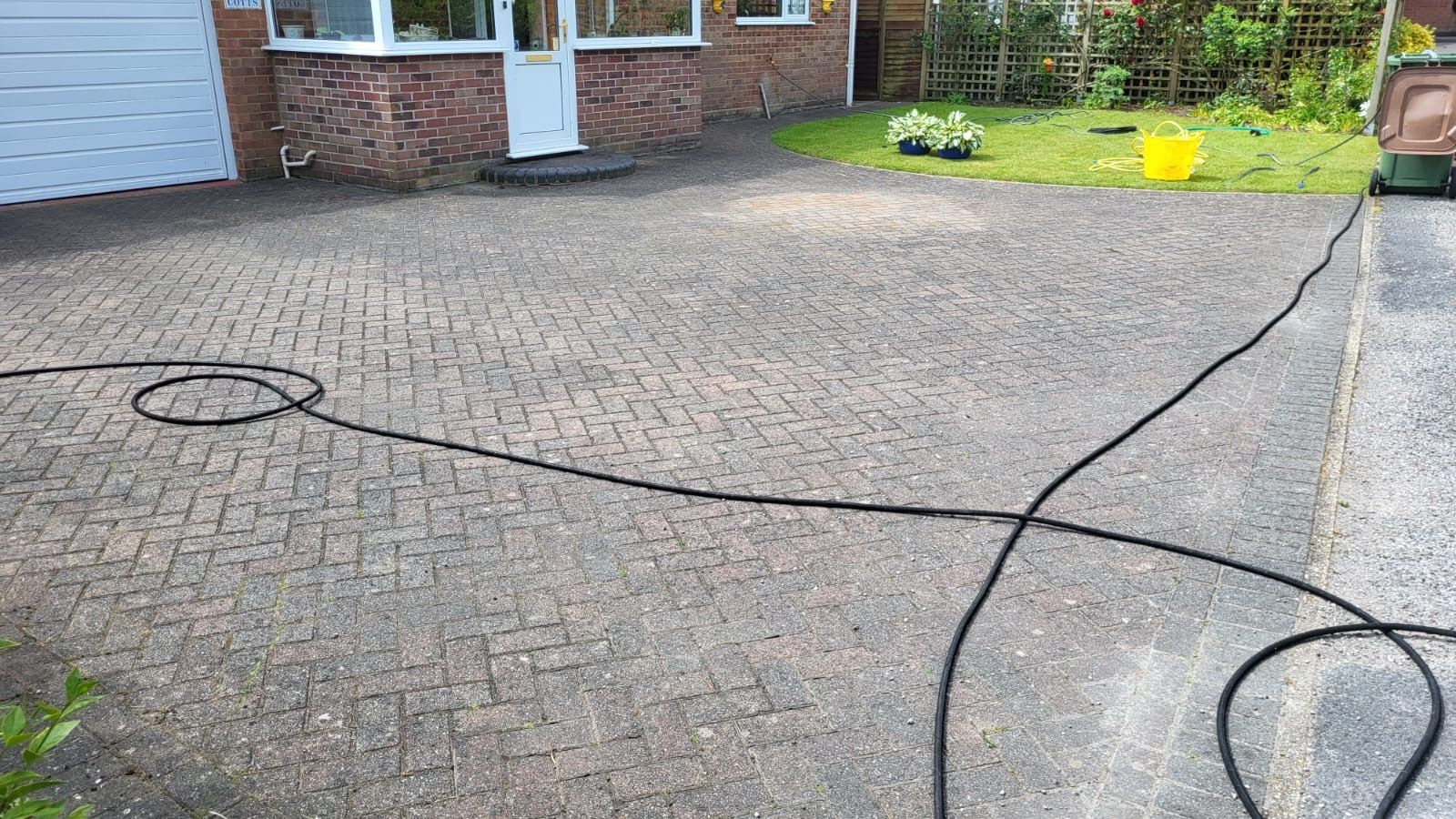 A hose is being used to clean a driveway in front of a house.