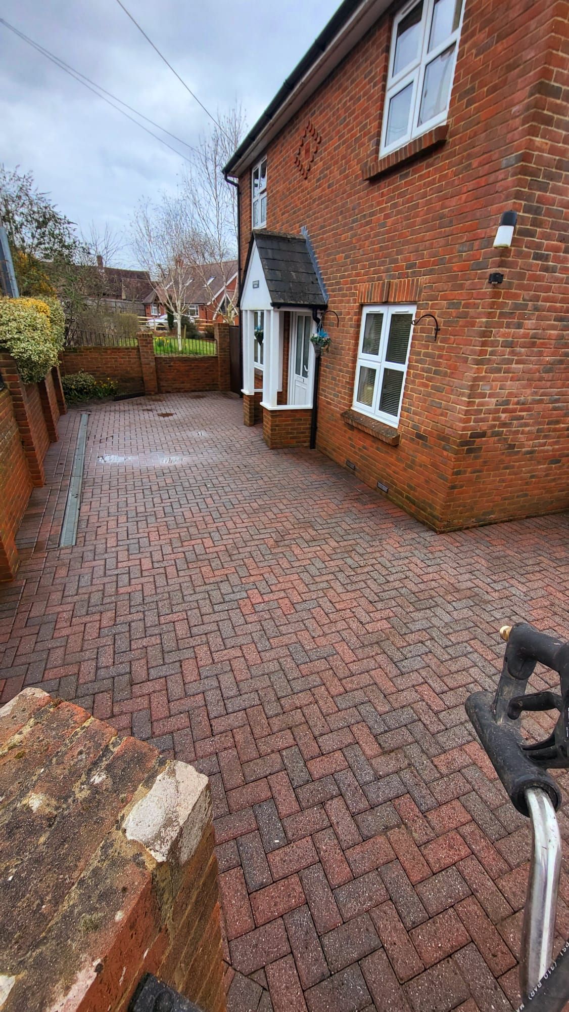 A clean brick driveway leading to a brick house with a bicycle parked in front of it.