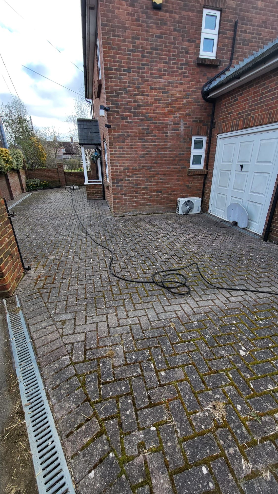 A dirty brick driveway leading to a brick house with a garage.