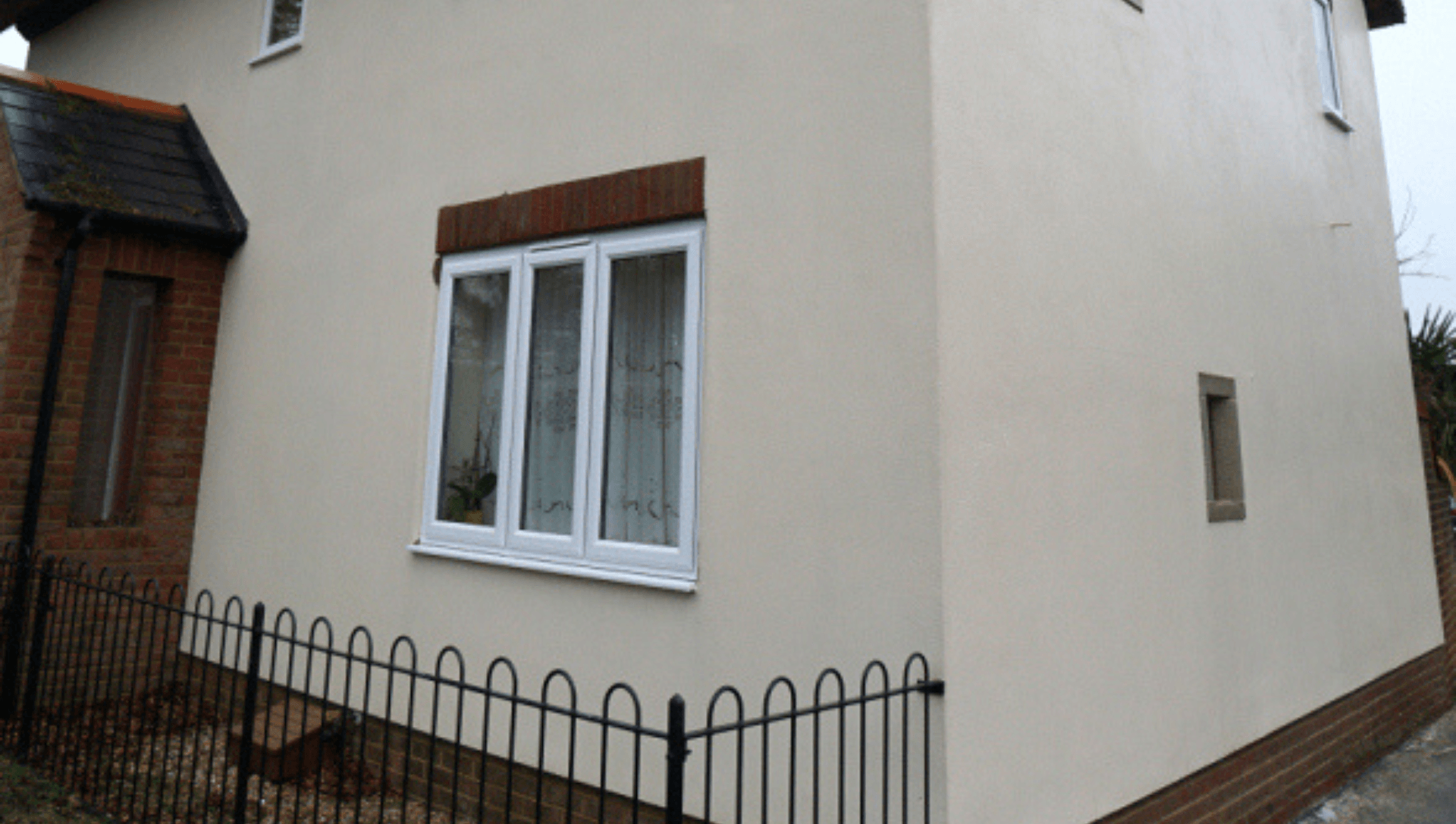 A clean white house with three windows and a fence around it.