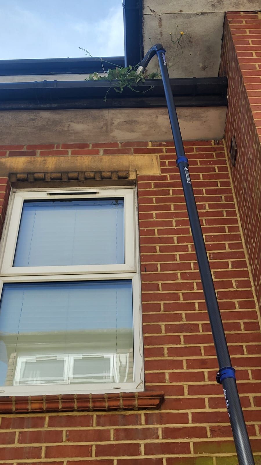 A gutter is being cleaned on the side of a brick building.
