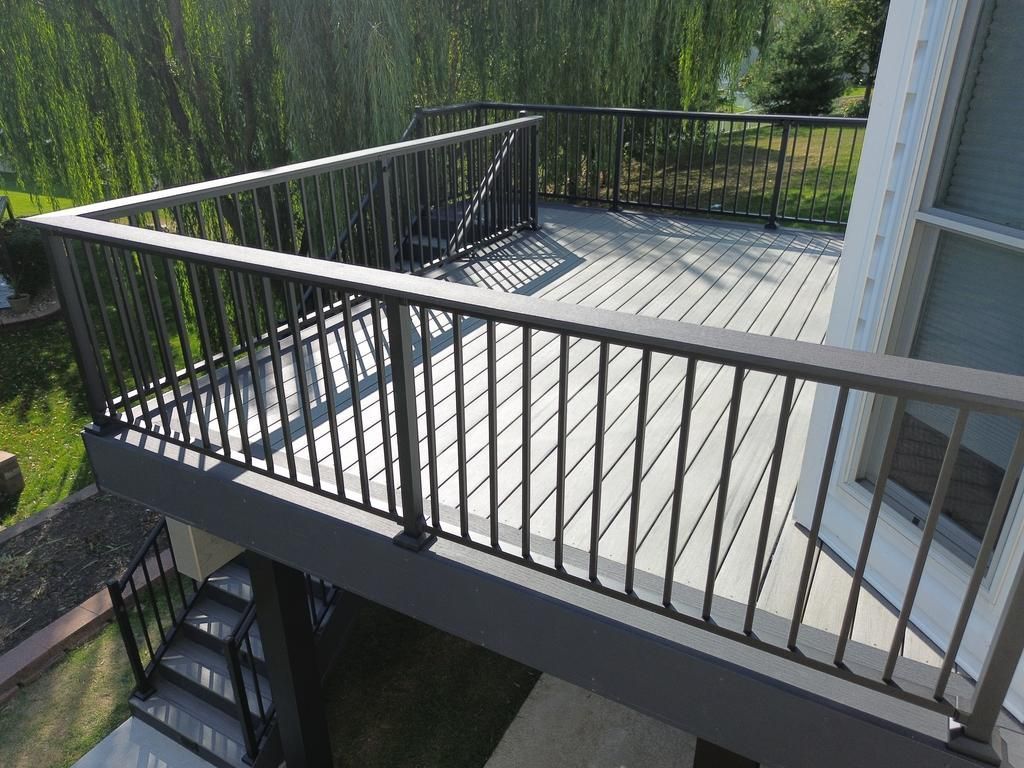 Deck with dark gray railing and composite decking, attached to a house with a willow tree background.