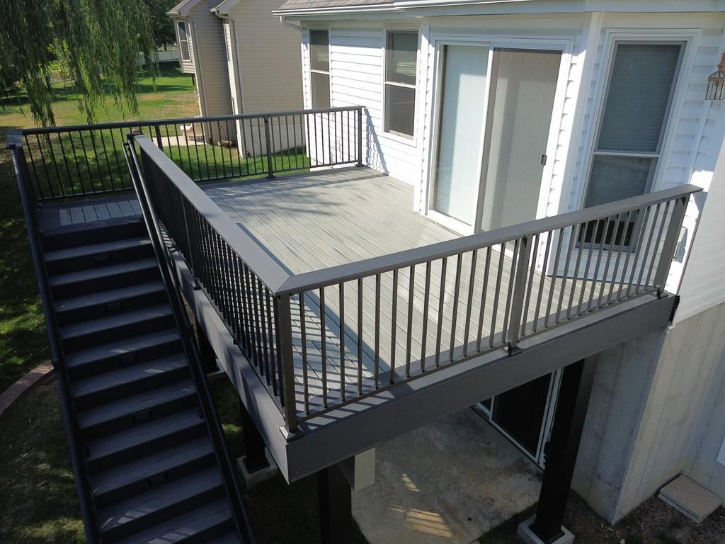 Gray deck with black railing and stairs attached to a white house.