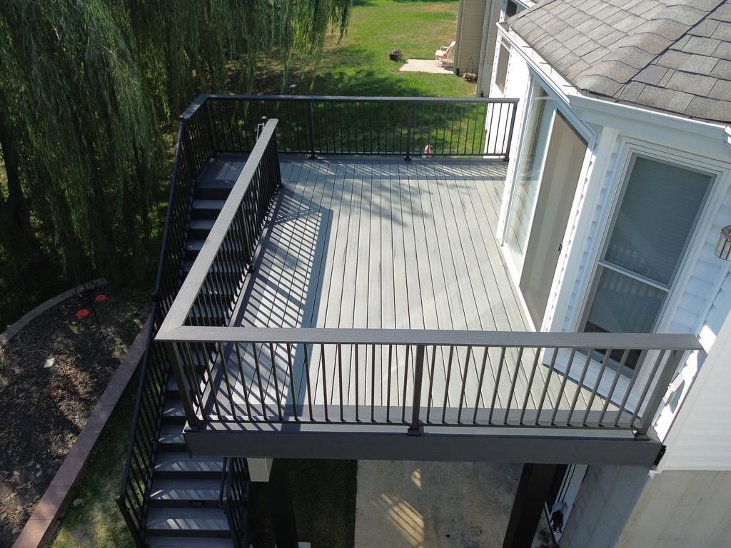 Elevated deck with dark railing and stairs; next to a white house with a screened door.