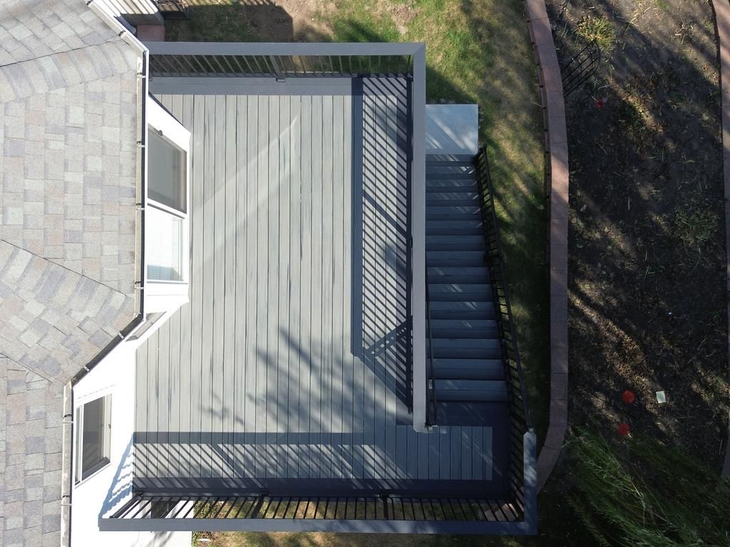 Overhead view of a gray composite deck with stairs leading to a yard, attached to a house with a shingled roof.