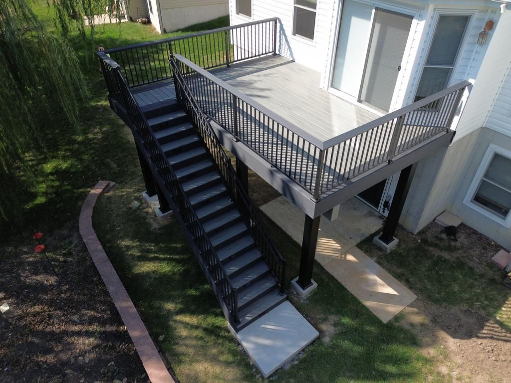 Black deck with stairs attached to a house with white siding and a grassy yard.