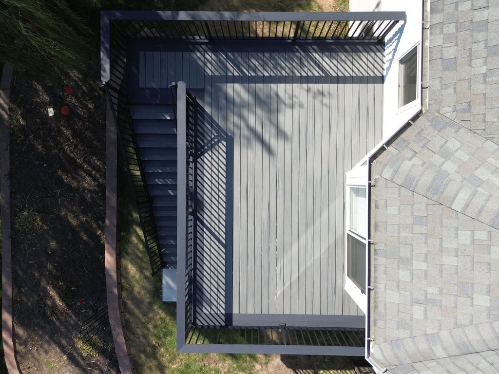 Aerial view of a gray composite deck attached to a house with a dark gray railing and steps.