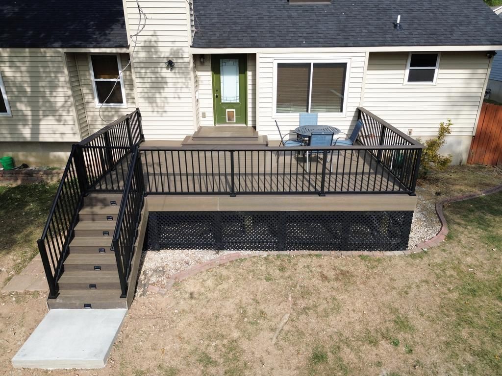A deck with black railings and stairs. Beige house with green door. Patio furniture visible.