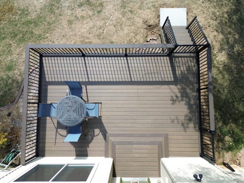 Overhead view of a deck with a dark-colored pergola and a table with chairs. Stairs lead up to the deck.