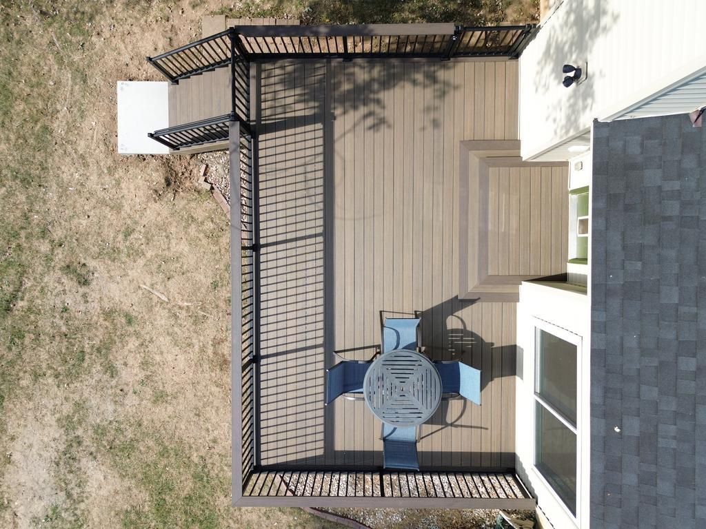 Overhead view of a composite deck with a table and chairs. Black railings surround the deck, with a house on the right.