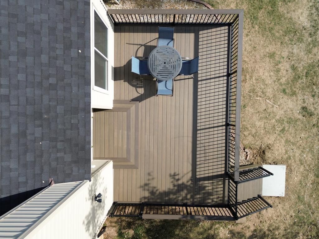 Aerial view of a brown composite deck with a table, chairs, and railing next to a house.