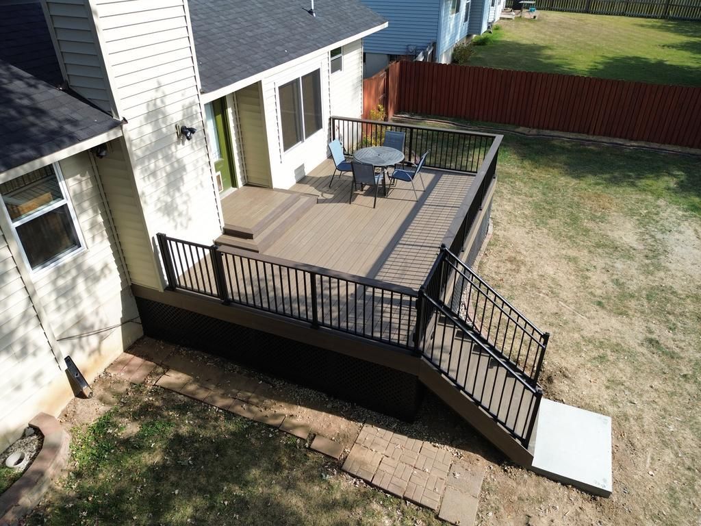 Brown deck with black railing and steps leading to a yard with a table and chairs.