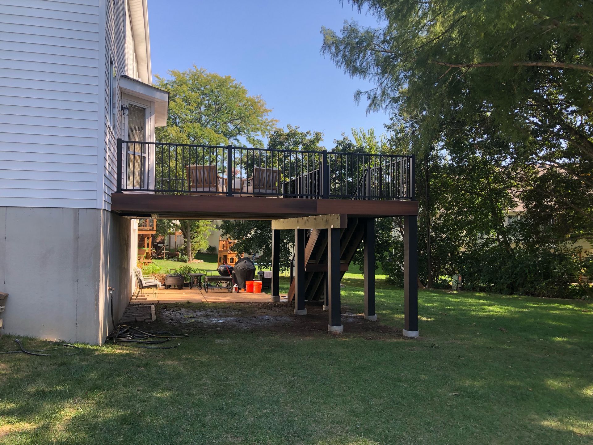 Deck attached to a house with black railings, supported by black posts, in a grassy backyard.