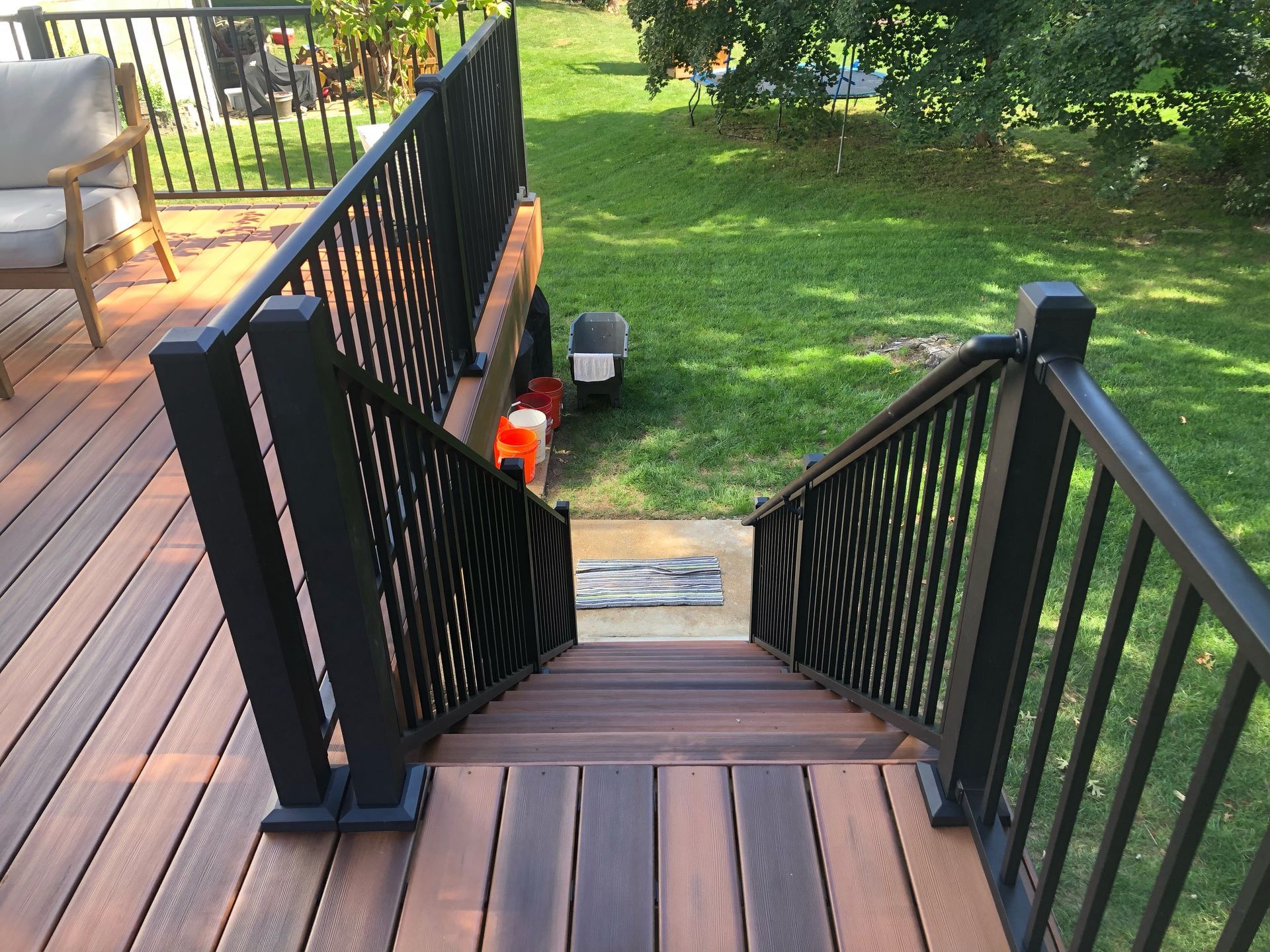 Wooden deck with black railings and steps leading to a grassy yard.