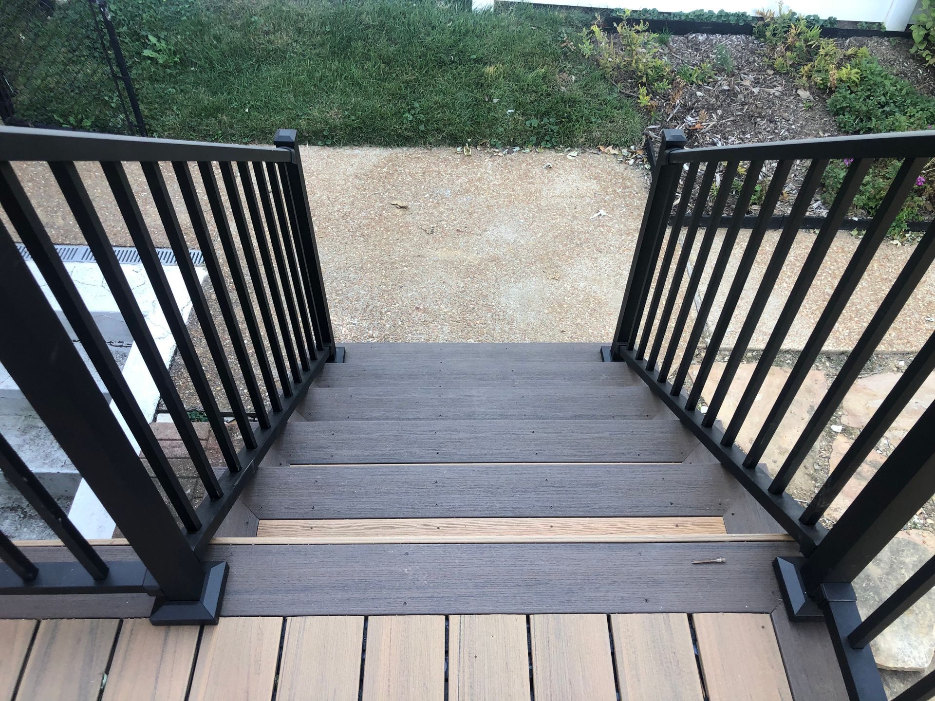 Staircase with black railing leading to a concrete path, surrounded by grass and vegetation.