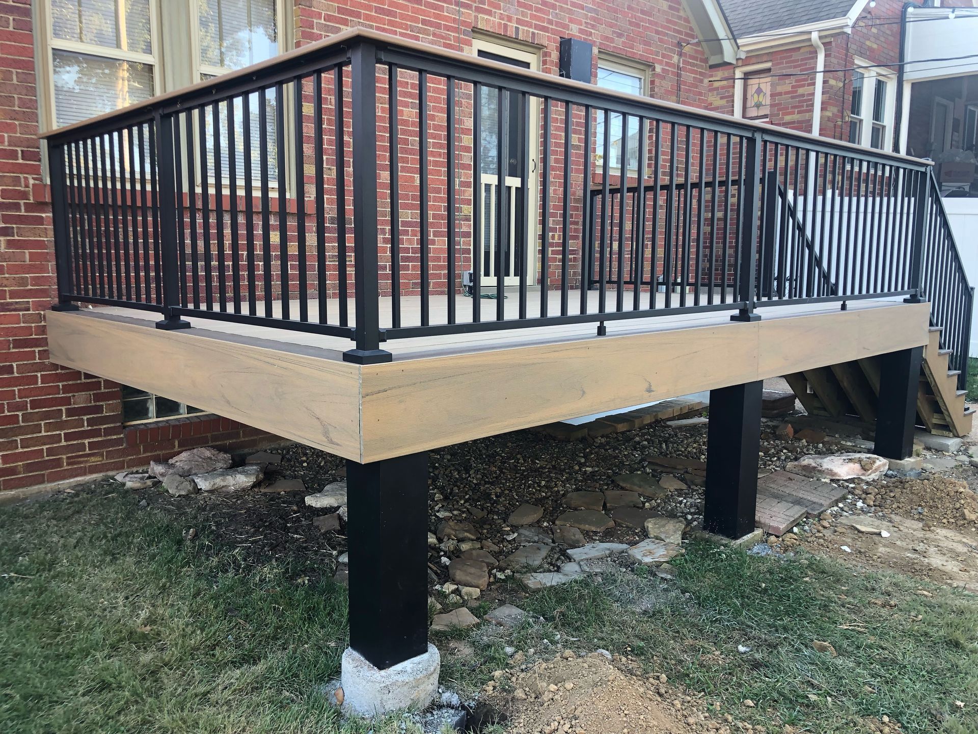 Wooden deck with black metal railing, supported by black posts on concrete.
