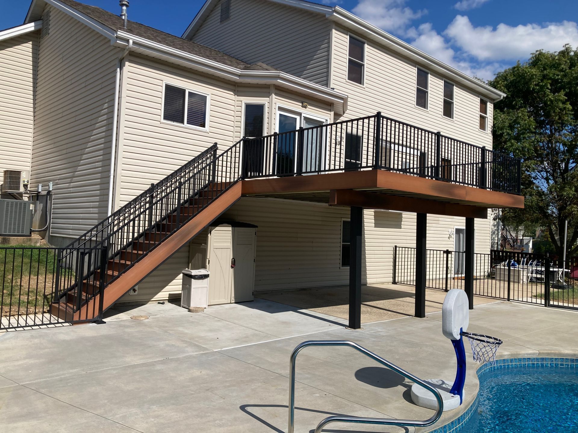 Two-story house with a wooden deck and black railing overlooking a swimming pool.