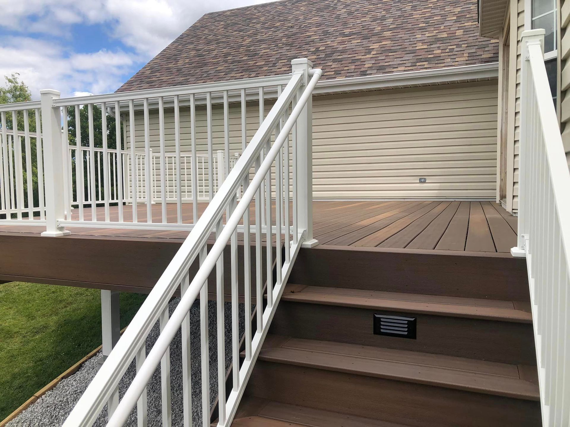 Brown composite deck with white railings, steps leading up. Back of house visible.