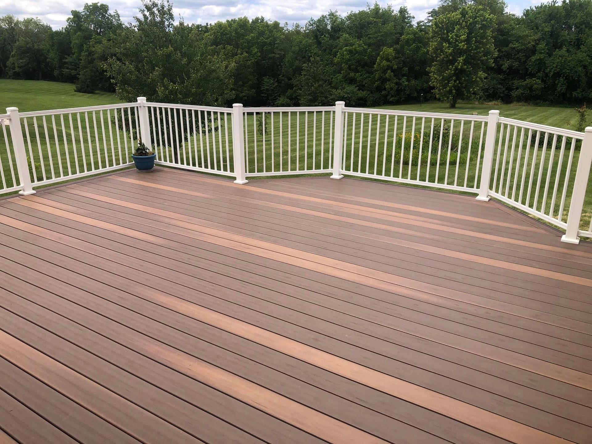 Wooden deck with white railings overlooks a grassy area and trees.