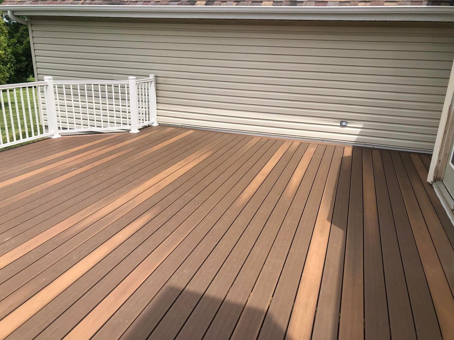 Wooden deck with white railing against a light-colored building.