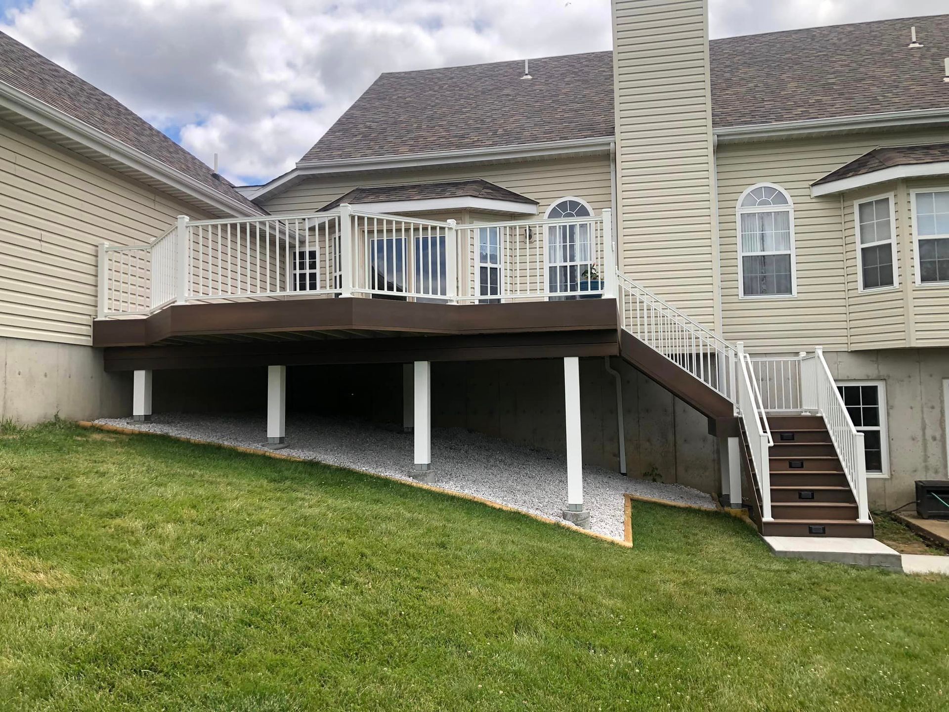 A multi-level deck on a house with white railing and brown decking; a grassy yard slopes down.