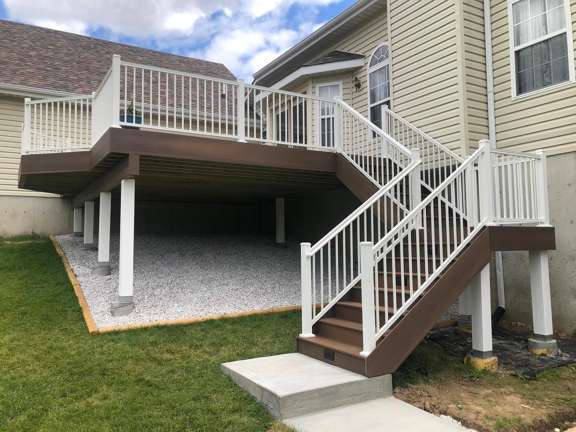 Backyard deck with white railing, brown decking, and stairs leading to a concrete pathway.