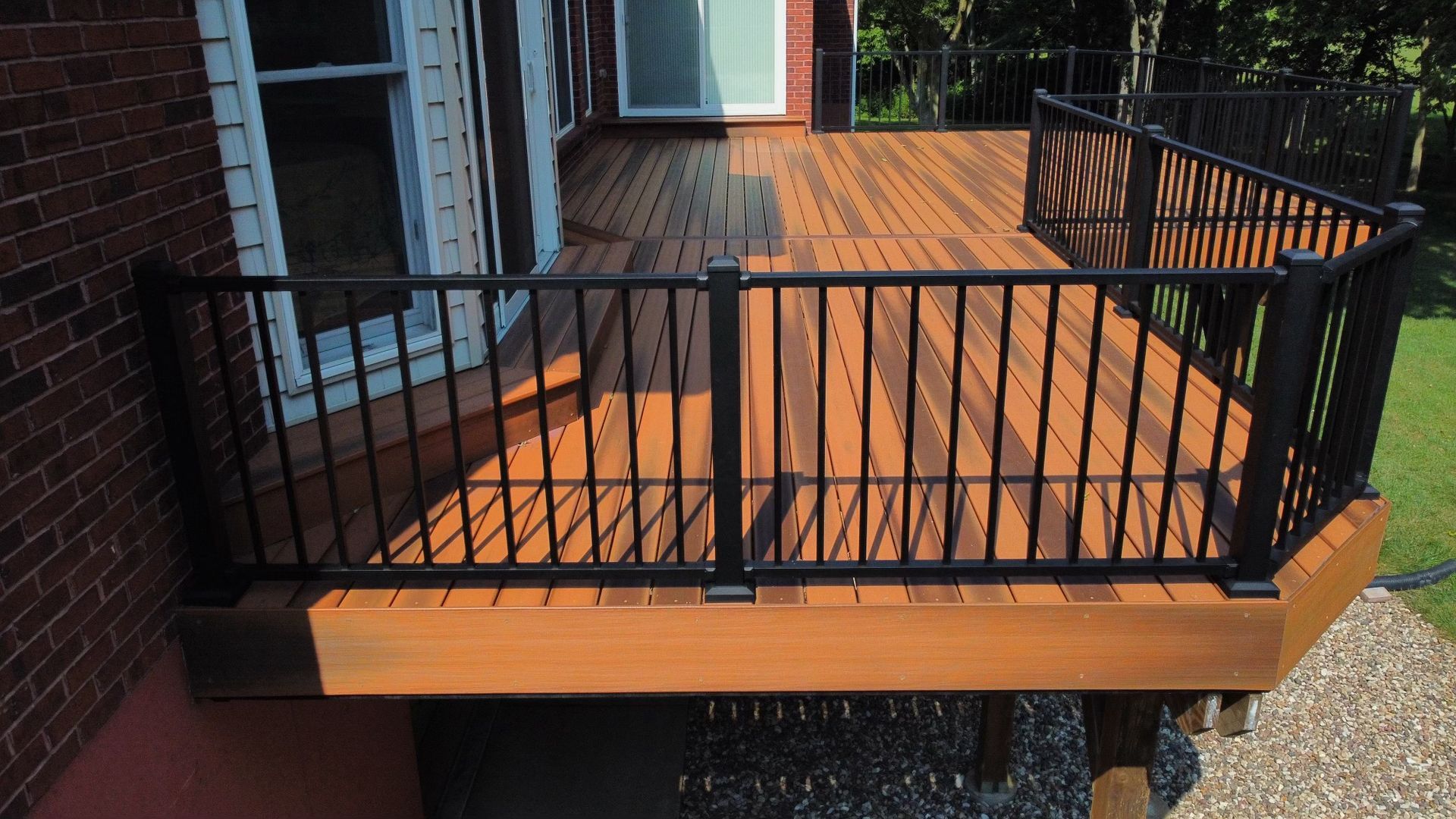 Wooden deck with black railing overlooking a yard, attached to a brick house.