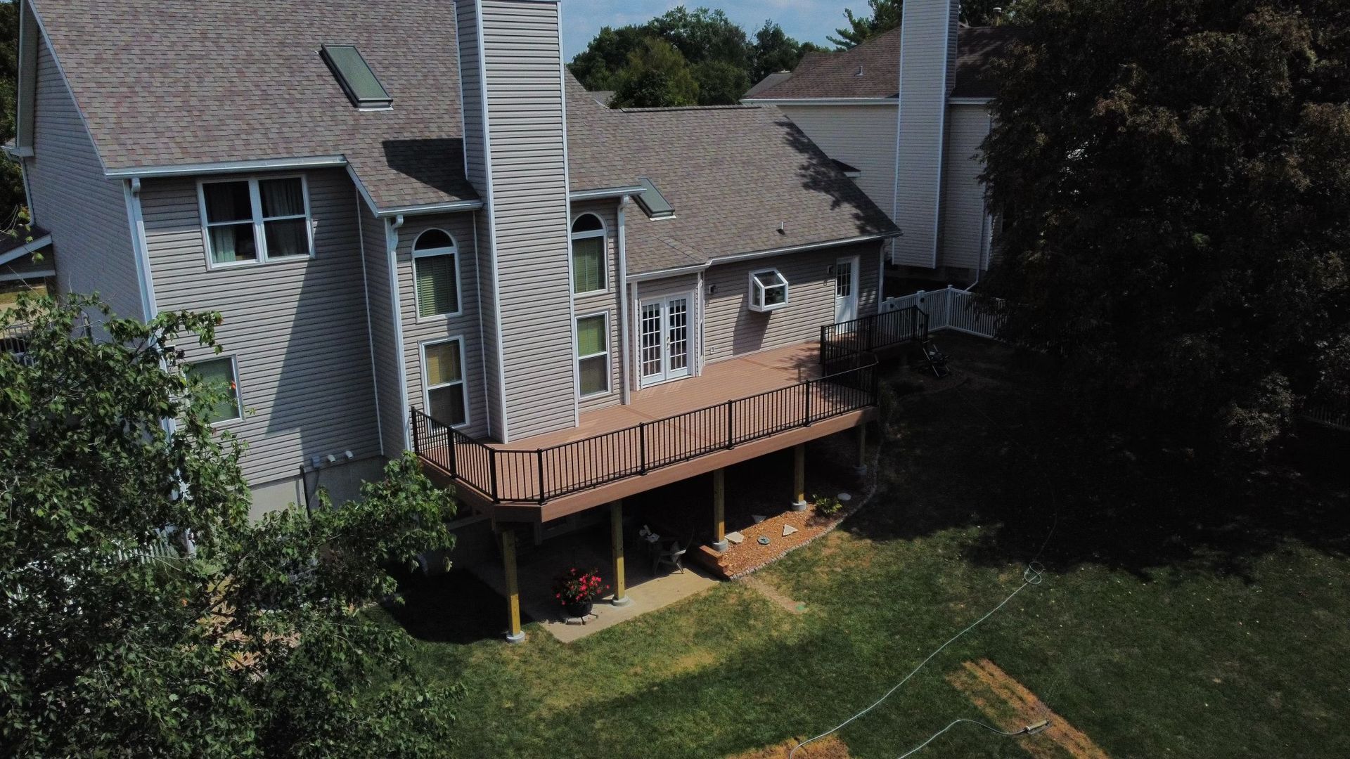 Two-story house with a wooden deck, a gray roof, and a grassy yard.