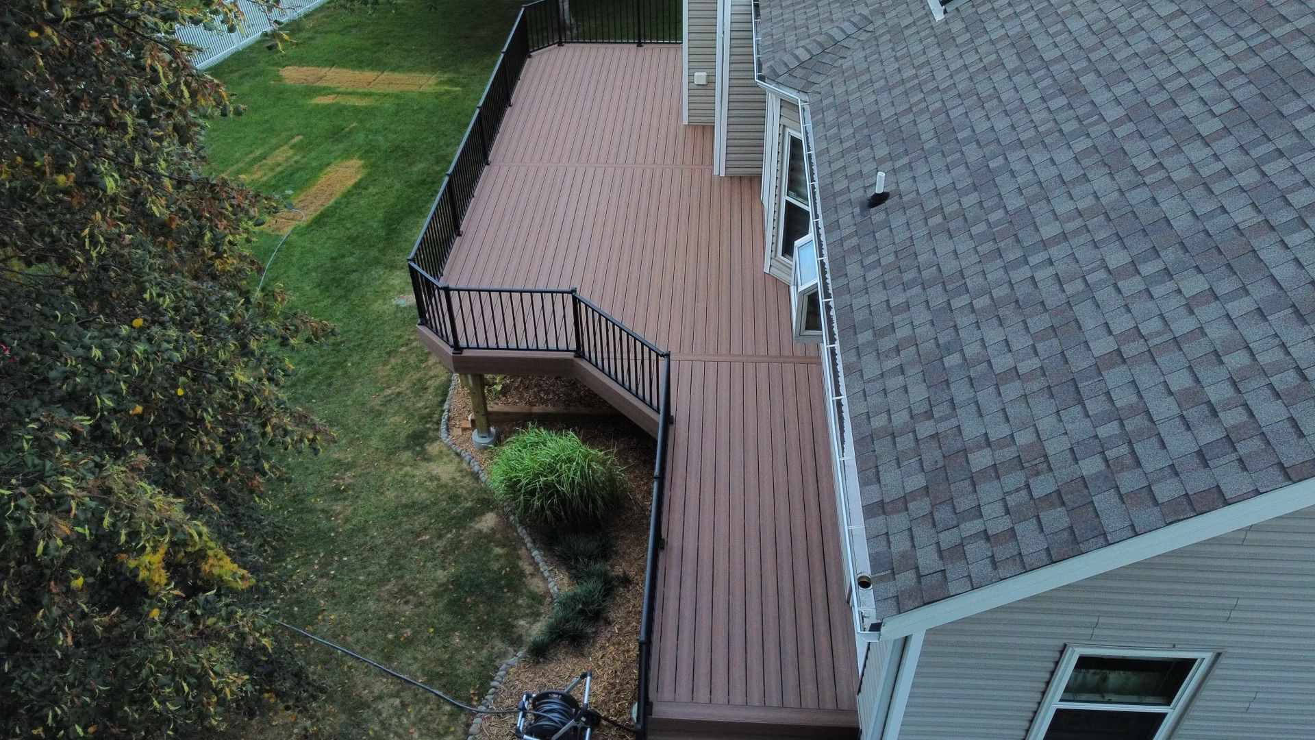 Overhead view of a house with a large brown deck and a gray shingled roof, set in a grassy yard.