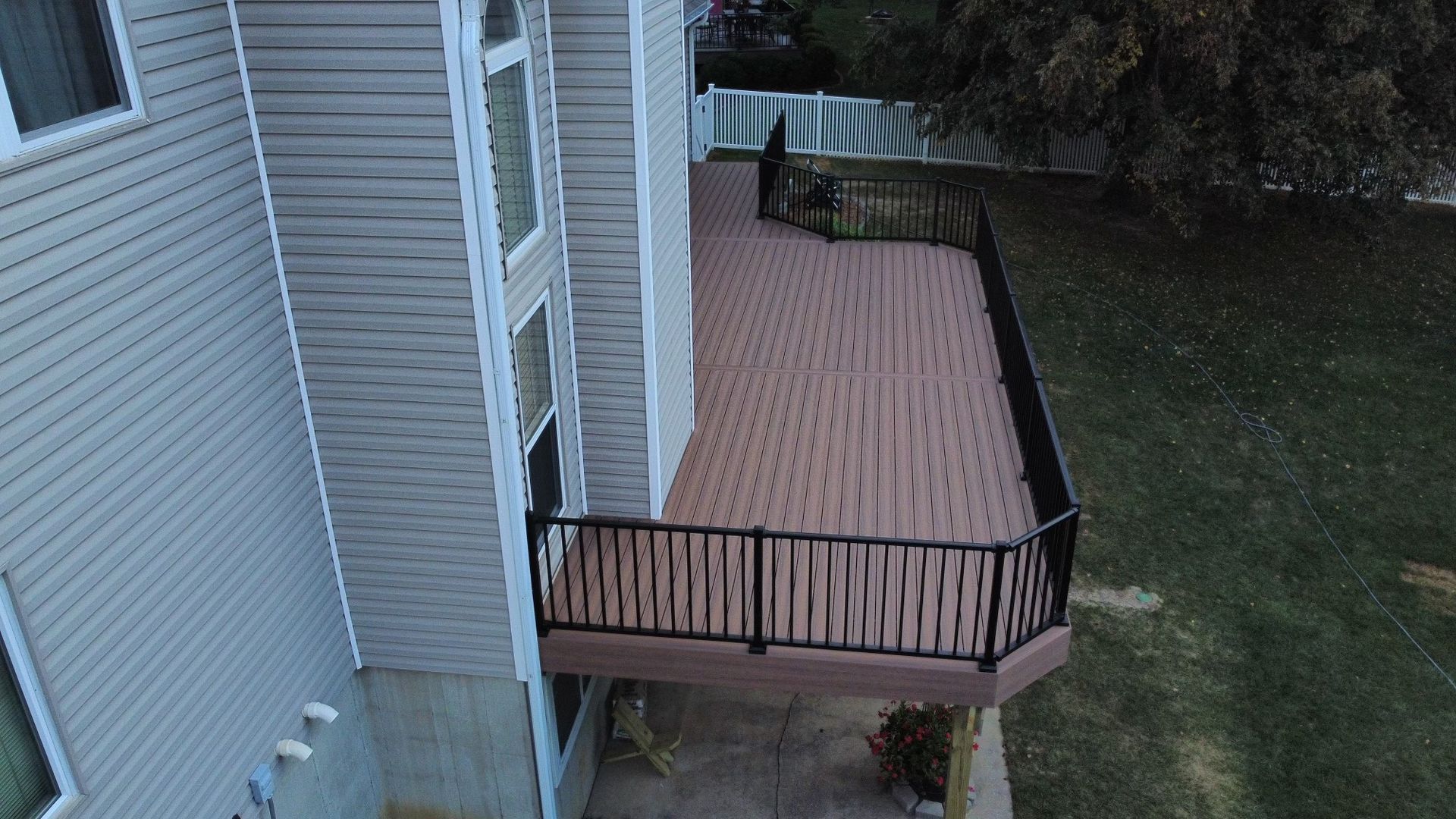 A multi-level composite deck with black railing is attached to a beige house, with a grassy lawn in the background.