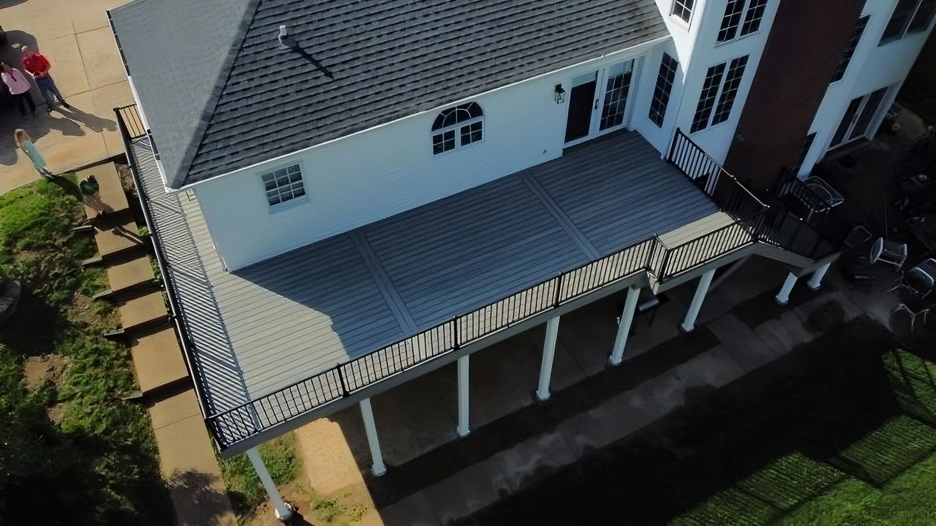 Aerial view of a white house with a gray deck and roof. A few people stand on a nearby path.