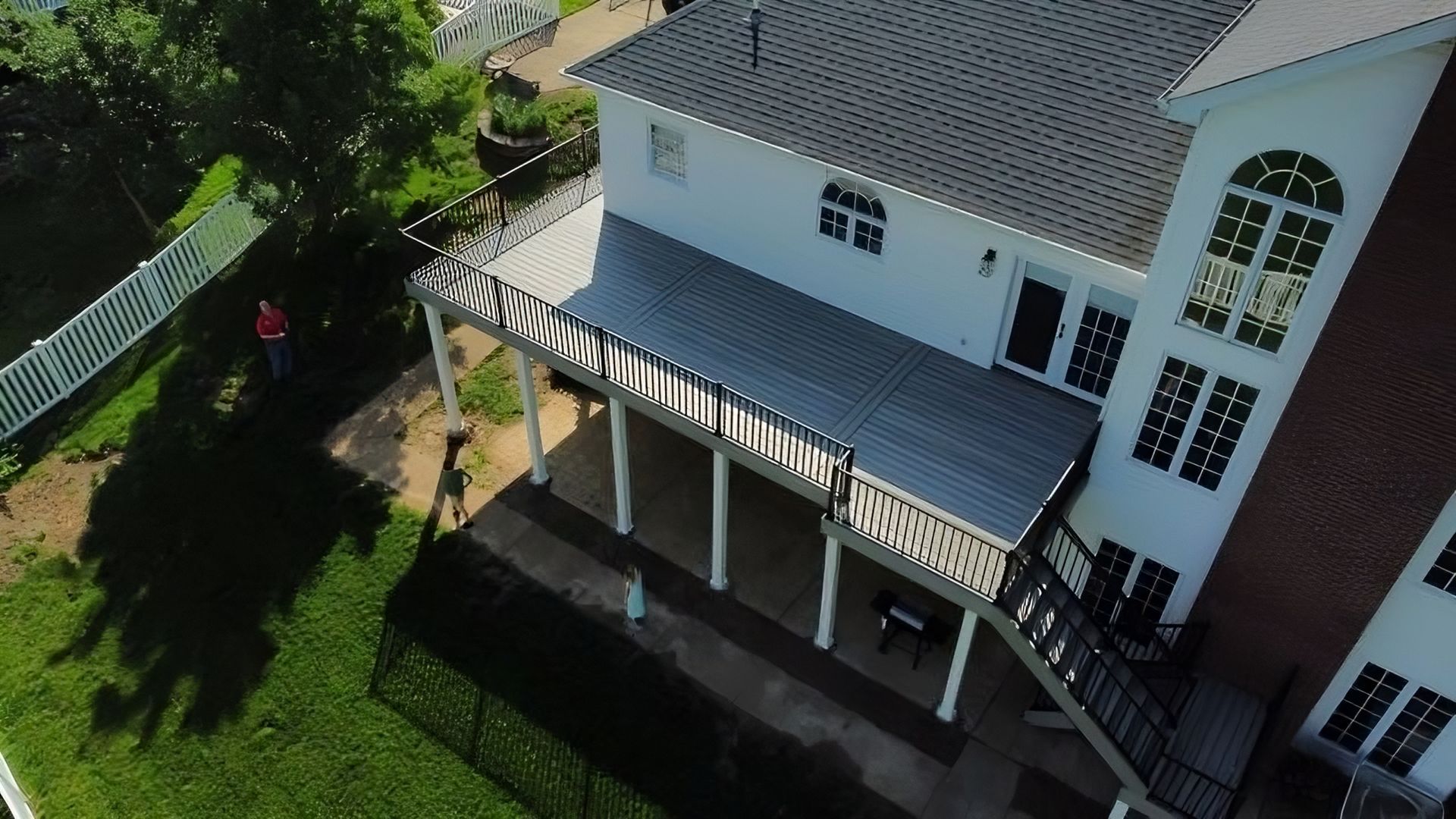Aerial view of a white house with a gray roof and large deck, person in the yard.