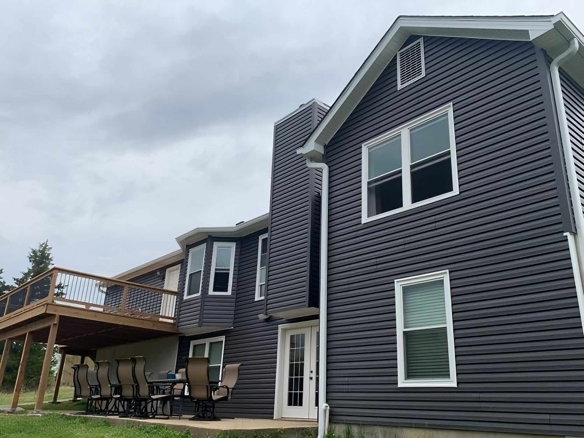 A large gray house with a deck and a table and chairs on it